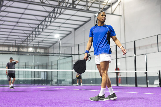 Diverse male athletes competing on covered purple turf court with paddle tennis rackets at net - Powered by Adobe