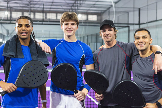 Diverse male friends in sportswear and standing with padel net on padel court, holding rackets - Powered by Adobe
