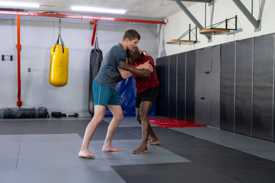 Diverse training partners grappling on foam mats in martial arts gym with hanging heavy bag