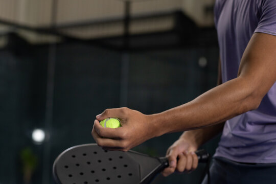 Male athlete holding yellow ball, pickleball paddle while wearing purple top on pickleball court
