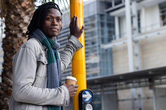 African american man leaning on yellow pole at street corner and sipping coffee, copy space