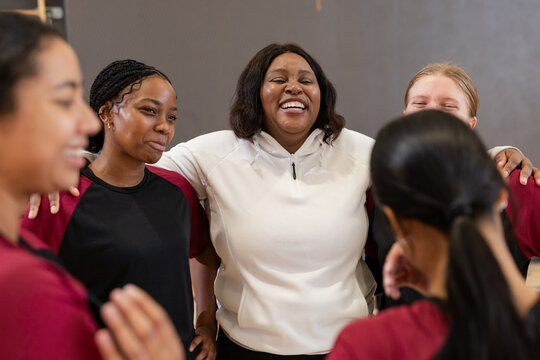 Diverse female team huddling on gym court wearing red and black jerseys, white training top - Powered by Adobe