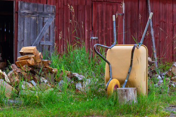 Yellow garden wheelbarrow with sawn firewood near storage. Preparing renewable wood fuel for winter heating. Eco-friendly, sustainable rural lifestyle in Finland