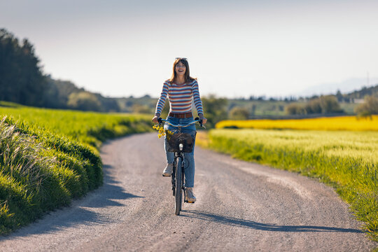 Smiling woman cycling on rural road surrounded by green fields