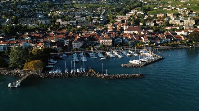 Aerial view of Lutry's harbor, where white boats contrast with the deep blue water, and red-roofed buildings meet the green landscape, Lutry, Vaud, Switzerland.