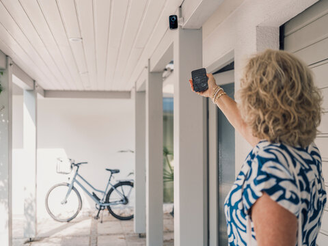 Woman using smartphone app to control home security camera outdoors