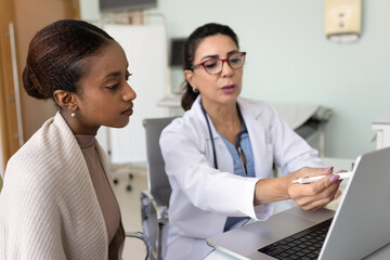Obraz premium Mature female doctor show medical information to patient on laptop