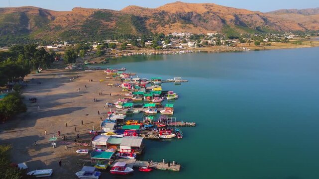 Aerial view of colorful boats docked at the shore of Khanpur Lake, where mountains meet the water's edge, creating a scenic contrast, Khanpur, Khyber Pakhtunkhwa, Pakistan.
