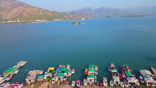 Aerial view of colourful boats docked at the edge of the serene Khanpur Lake, reflecting the clear blue sky, Khanpur, Khyber Pakhtunkhwa, Pakistan.