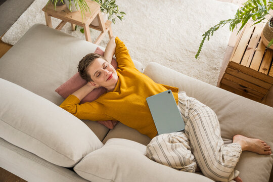 Woman smiling and relaxing on sofa with tablet at home