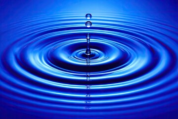 A single drop of water impacting a deep blue surface, creating concentric ripples