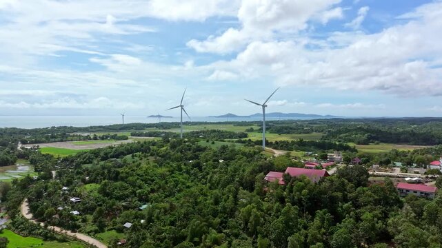 Aerial view of wind turbines standing tall amidst lush greenery and buildings, creating a striking contrast against the backdrop of the ocean, San Lorenzo, Western Visayas, Philippines.