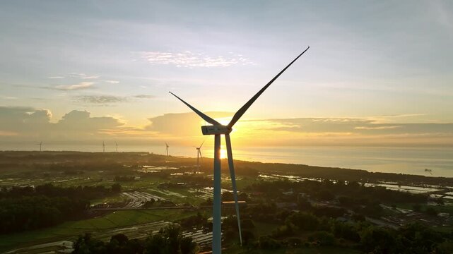 Aerial view of windmills standing tall against a vibrant sunset over the ocean and lush green fields, Guimaras, Western Visayas, Philippines.