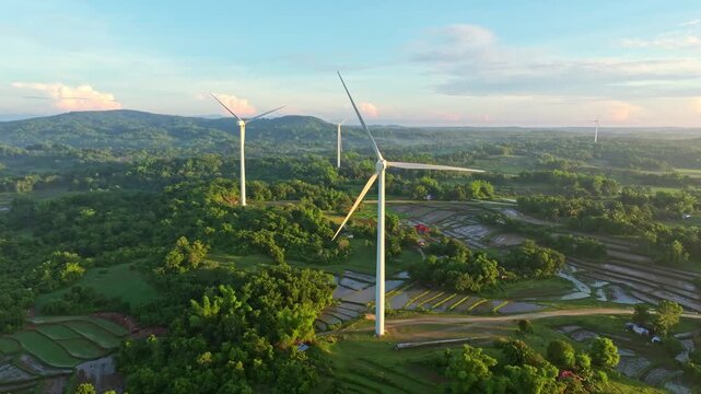 Aerial view of towering wind turbines stand amidst lush green hills and rice paddies, creating a striking contrast of modern energy and nature, Guimaras, Western Visayas, Philippines.