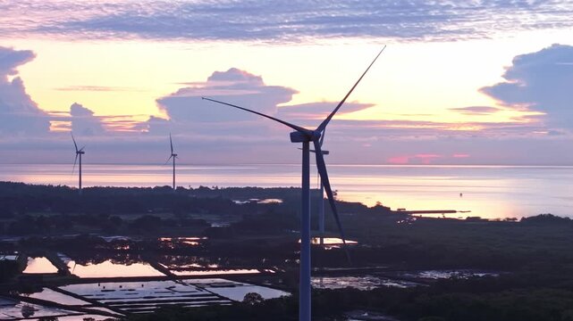 Aerial view of wind turbines standing tall against a sunset sky, their forms reflected in the still water below, Guimaras, San Lorenzo, Philippines.