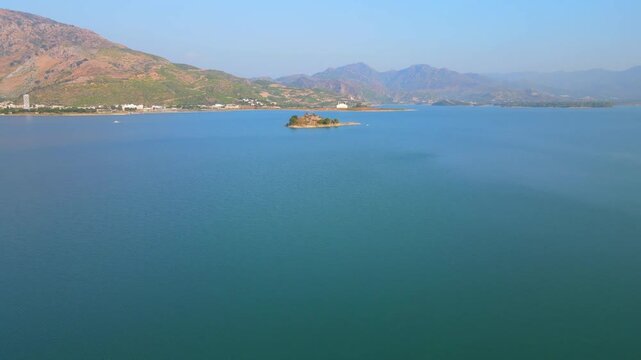 Aerial view of Khanpur Lake, its turquoise waters contrasting with the distant mountains and the small island in the center, Khanpur Lake, Khyber Pakhtunkhwa, Pakistan.