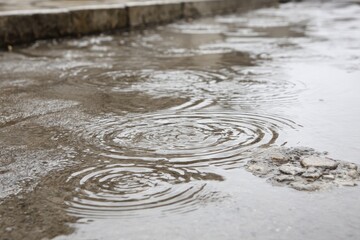 Rain-slicked pavement with circular ripples in puddles