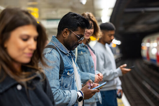 Commuters waiting on London underground platform using mobile phones