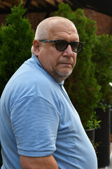 Portrait of an elderly gray-haired Caucasian man with a beard, wearing sunglasses and a blue T-shirt.