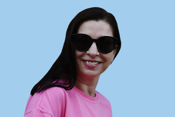 Portrait of caucasian brunette woman in sunglasses and pink t-shirt on blue background.