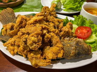 A delicious plate of crispy fried fish served with fresh lettuce, tomato slices, and a flavorful dipping sauce, perfect for a satisfying meal.
