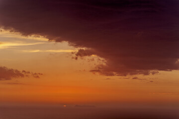 Olympos, Karpathos , Greece,  rolling hills and mountains beneath a vibrant orange sky. soft gradients of orange and pink with scattered clouds, during sunset