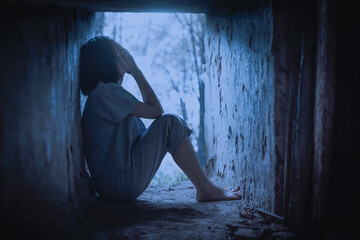 A scared young girl covers her face with her hands in basement apartment at night. Kidnapping and human trafficking concept