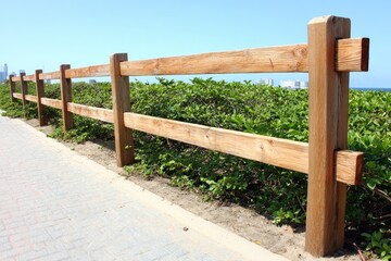 Fototapeta premium Wooden fence bordering a walkway and lush greenery