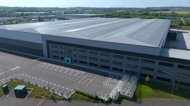Nottingham, United Kingdom - 10 August 2025: Aerial view of a vast warehouse with rows of windows and an empty parking lot on a clear day.