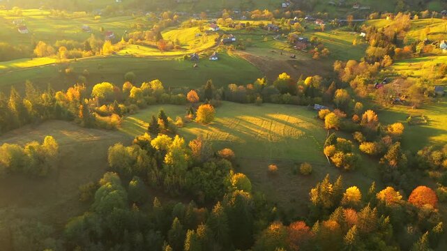 A drone flies over a village in a hilly area with autumn trees glowing in the sun. Carpathian mountains, Ukraine, Europe. UHD 4k video.