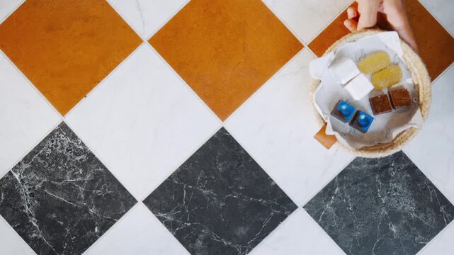 A basket of assorted soaps and lotions sits on a tile floor. The basket is placed on a tile floor with a checkered pattern