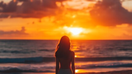 Fototapeta premium Silhouette of a woman gazing at a vibrant sunset over the ocean
