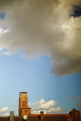 Red brick clock tower with a red roof and golden detail against a blue sky with dramatic white clouds. Scenic architecture view on a sunny day.