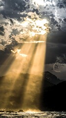 Golden rays pierce through stormy clouds, illuminating a dramatic coastal scene.