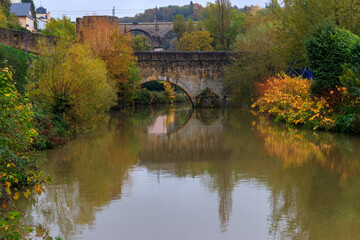 Fototapeta premium Small stone arched bridge across the Alzette River in the Grund, lower part of Luxembourg city, Luxembourg. Scenic autumn landscape
