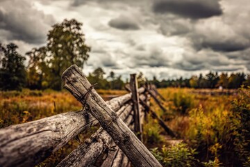 Rustic wooden fence stretches into a field under a stormy sky
