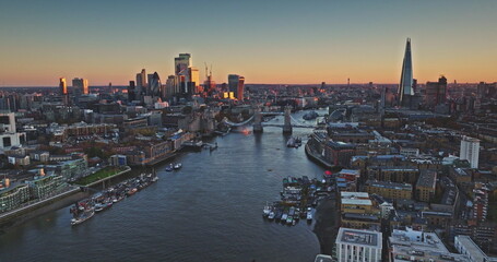 Tower Bridge and The Shard are reflecting on River Thames at sunset, creating a stunning cityscape view of London's business district. Evening city skyline under vibrant sky. Drone flight