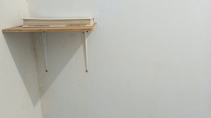A minimalist wooden wall shelf with white metal supports, mounted on a plain wall with a single book on top. A simple and functional concept for a home or workspace interior.