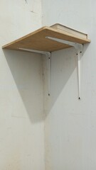 A minimalist wooden wall shelf with white metal supports, mounted on a plain wall with a single book on top. A simple and functional concept for a home or workspace interior.