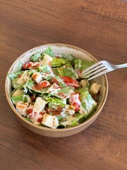 A Close-Up View of a Fresh, Appetizing Garden Salad, featuring Bright Green Lettuce, Red Tomatoes, and Crispy Croutons, generously coated with a Creamy Dressing. Served in an Earthy Bowl on a Natural
