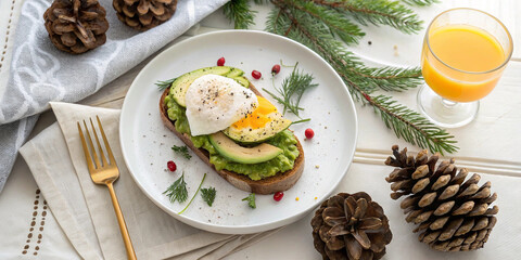 Festive holiday breakfast featuring avocado toast with poached egg and fresh dill accompanied by orange juice and pine cones on white wooden table.