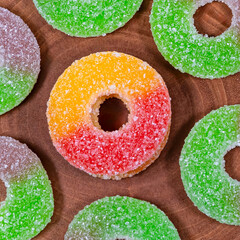 Colorful sugar-coated gummy rings arranged neatly on a rustic wooden background. Chewy, fruity candies with vibrant colors, ideal for desserts, sweet snacks, festive parties, and food advertising.