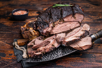 Slow ccoked sliced Venison leg, roasted game meat of deer on a board with herbs. wooden background. top view
