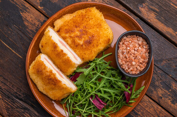 Chicken Fried cordon bleu cutlet on plate with salad. wooden background. top view