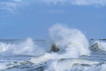 Puissantes vagues de l’océan Atlantique explosant en écume blanche sous un ciel bleu nuageux. Scène maritime naturelle et dramatique, symbole de la force de la mer.
