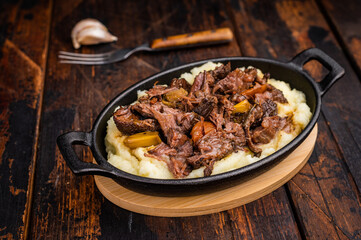 Braised Beef Cheek, Slow cooked meat with smashed potatoes in a skillet. wooden background. top view