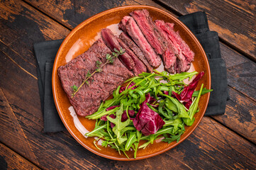 Grilled Skirt machete beef steak, roasted sliced meat on plate with salad. wooden background. top view