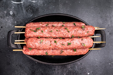 Raw shish kebab, arabic kofta kofte kebab from mince lamb and beef meat on Skewer. black background. top view