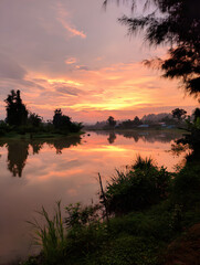 Reflective River at Sunrise with Orange Sky and Lush Greenery