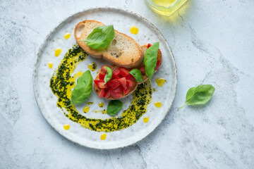 Plate with tomato bruschettas, basil oil and fresh basil on a white stone background, horizontal...